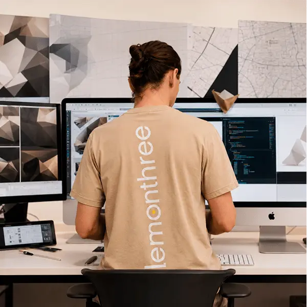 Designer wearing a lemonthree t-shirt building a website across three screens