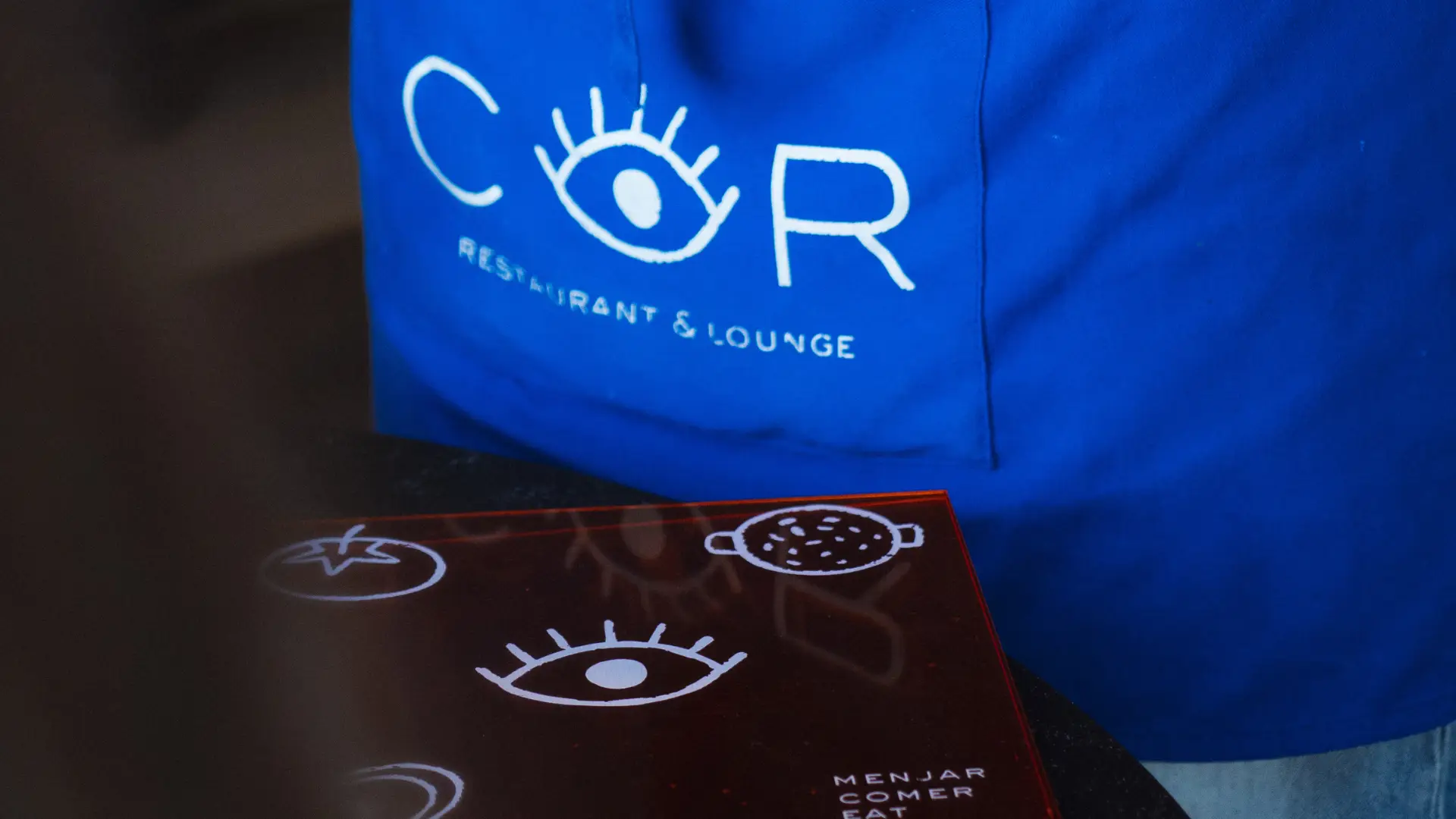 COR Restaurant & Lounge branded apron and menu with the restaurant's eye logo