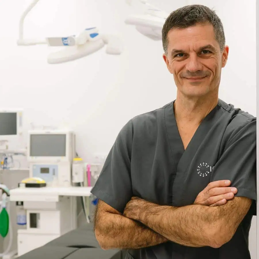 Dr. Thione in surgical scrubs, arms crossed, in the operating room